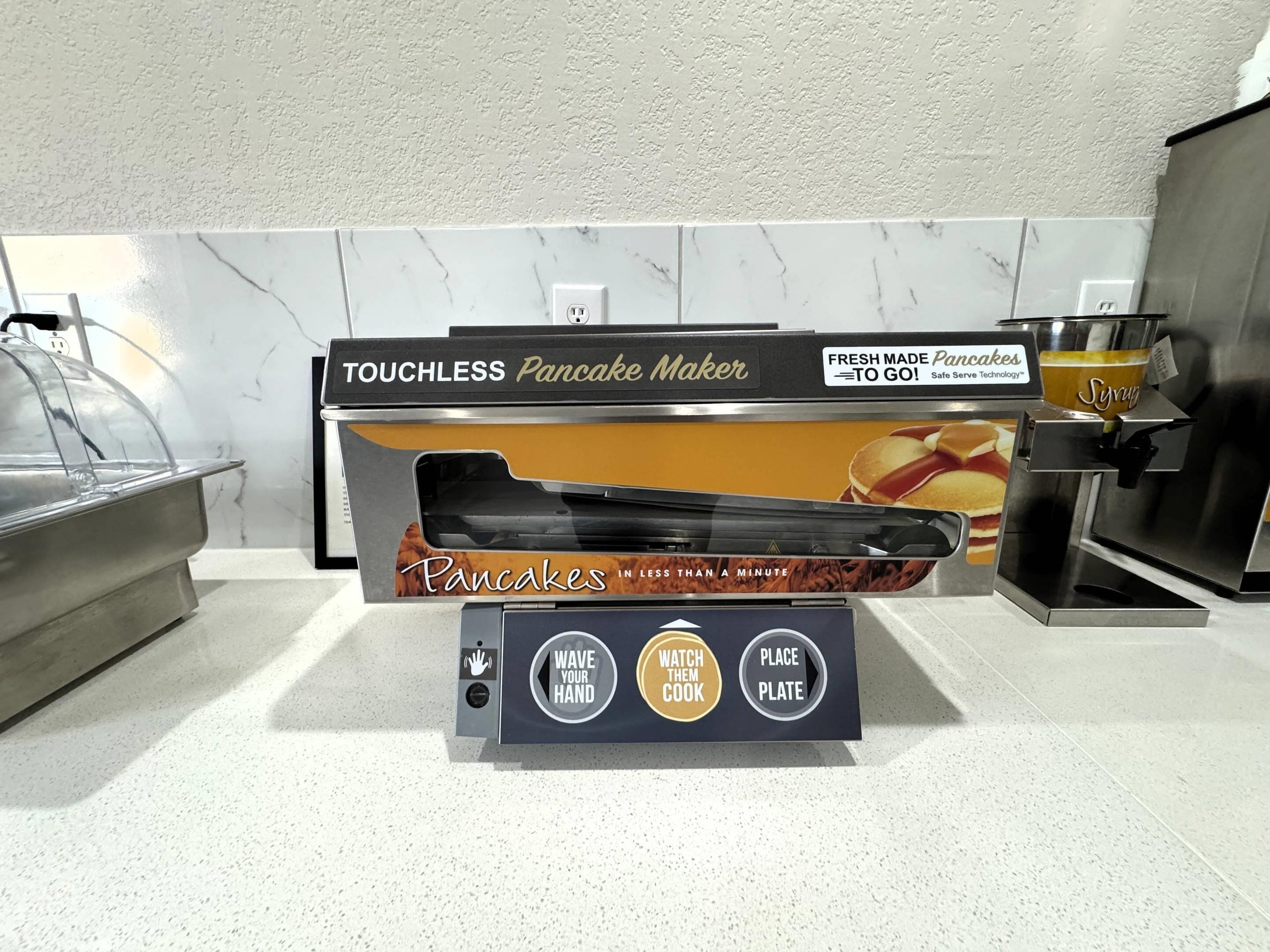 A touchless pancake maker with a packaging box, a syrup dispenser, and a handwashing station.