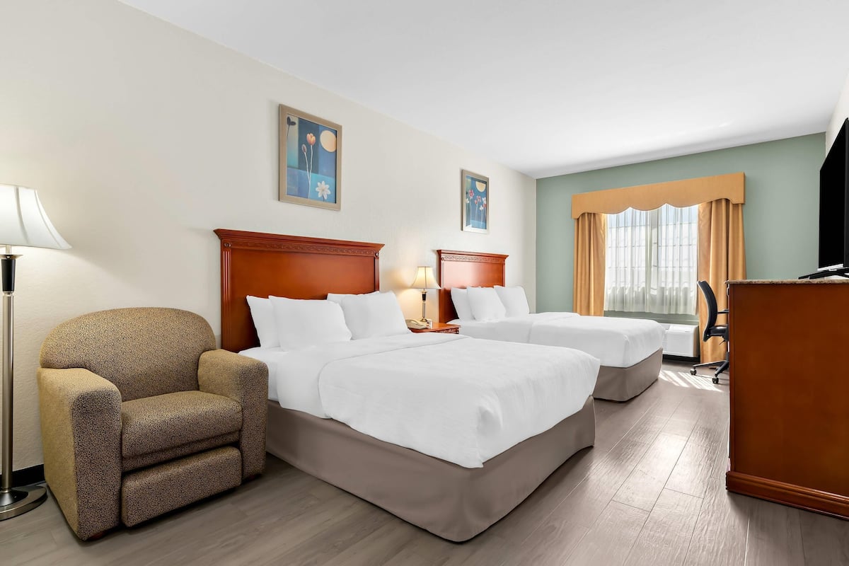 A hotel room with two beds, a chair, a desk, and a lamp.