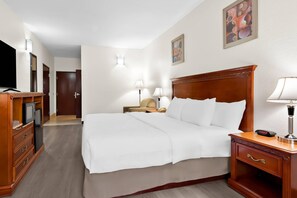 Habitación de hotel con una cama grande, televisión, escritorio con lámpara y mesita de noche con reloj.
