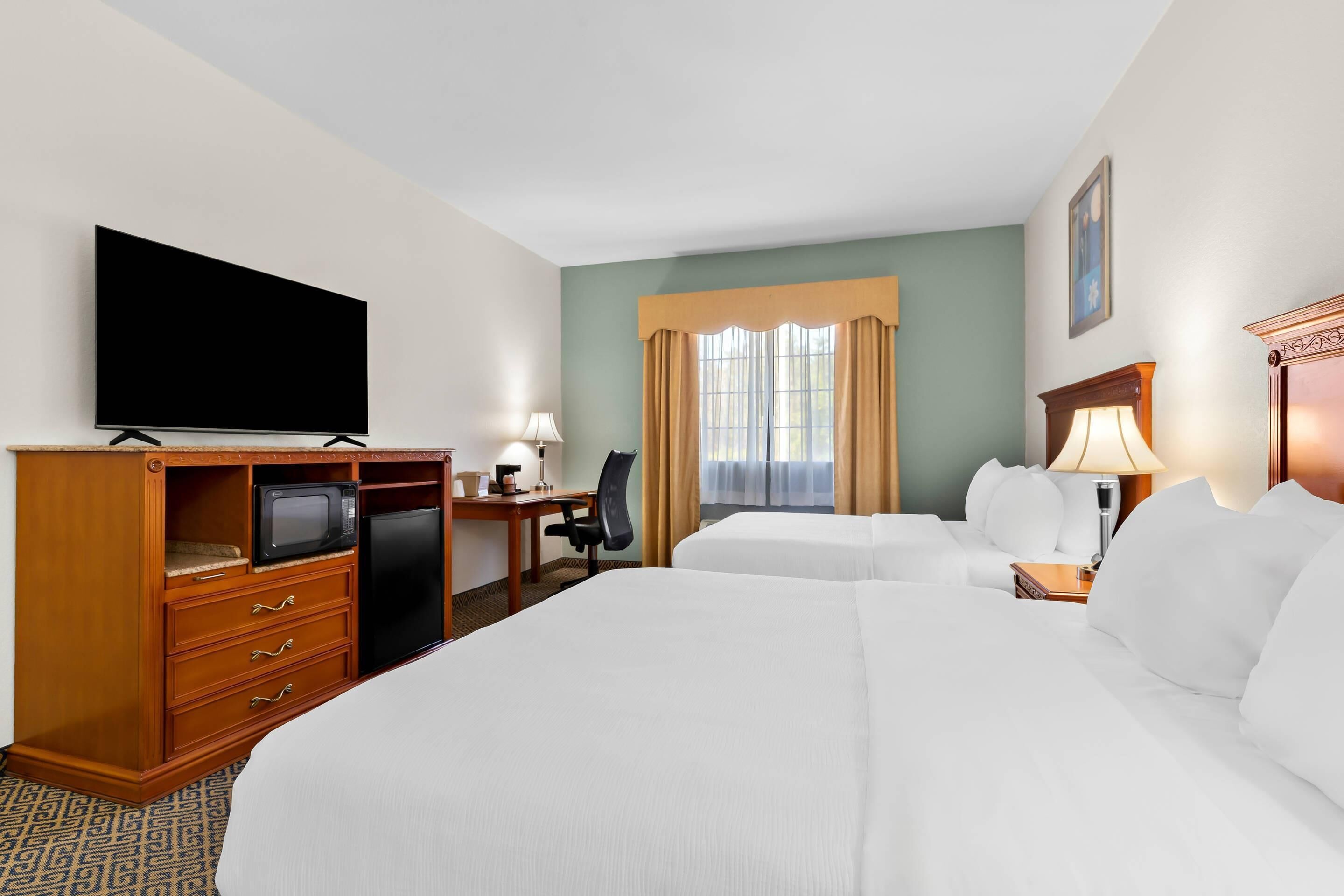 A hotel room with a large bed, a desk with a computer, a television, and a window with curtains.