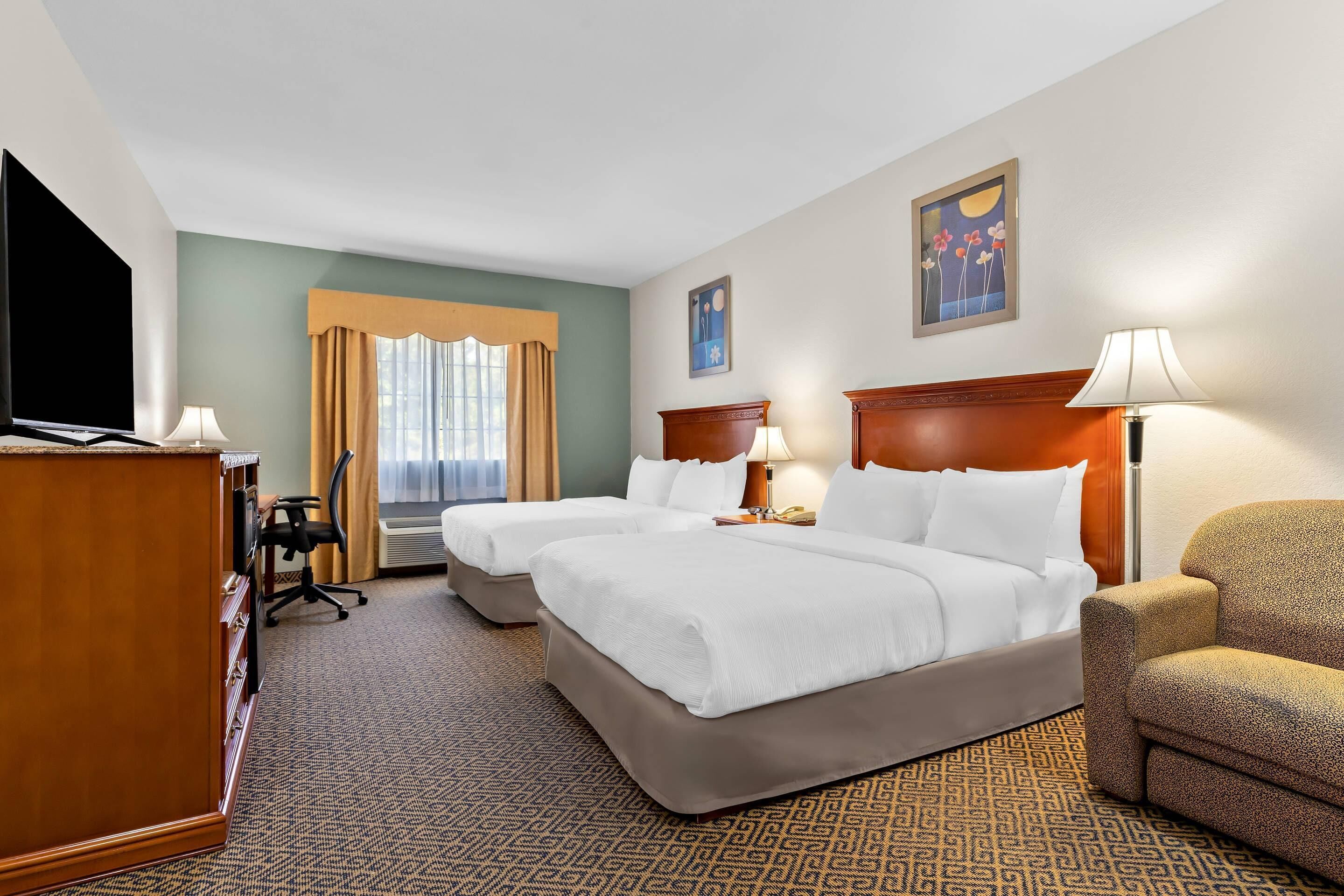 A hotel room with two beds, a desk, a chair, and a TV.