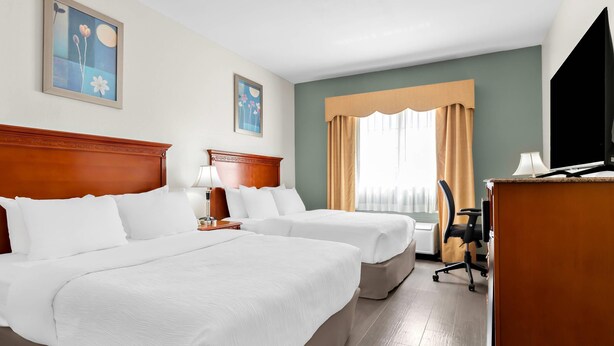 A hotel room with two beds, a desk, a chair, a TV, and artwork on the walls. - Quality Inn & Suites McAlester on Hwy 69 (McAlester)