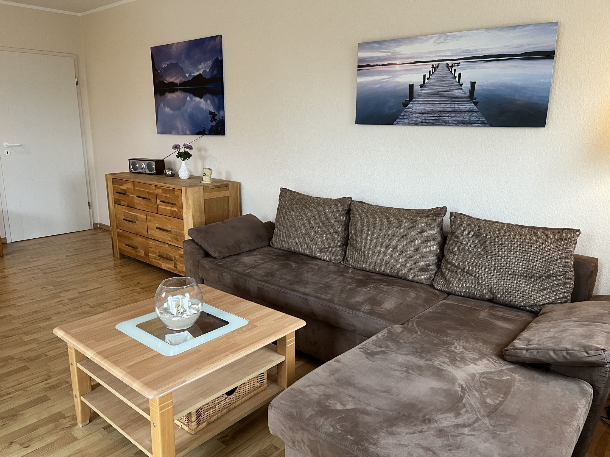 A living room with a brown sofa, wooden coffee table, and two paintings on the wall.