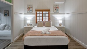 Ein Schlafzimmer mit einem großen Bett, zwei Nachttischen mit Lampen, einem Fenster mit Jalousien und einer grünen Wand links.