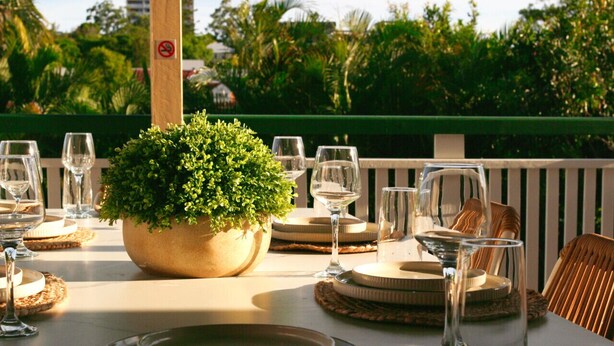Mesa lista para comer con un centro de mesa de planta en maceta, copas de cristal y protectores de mesa tejidos.