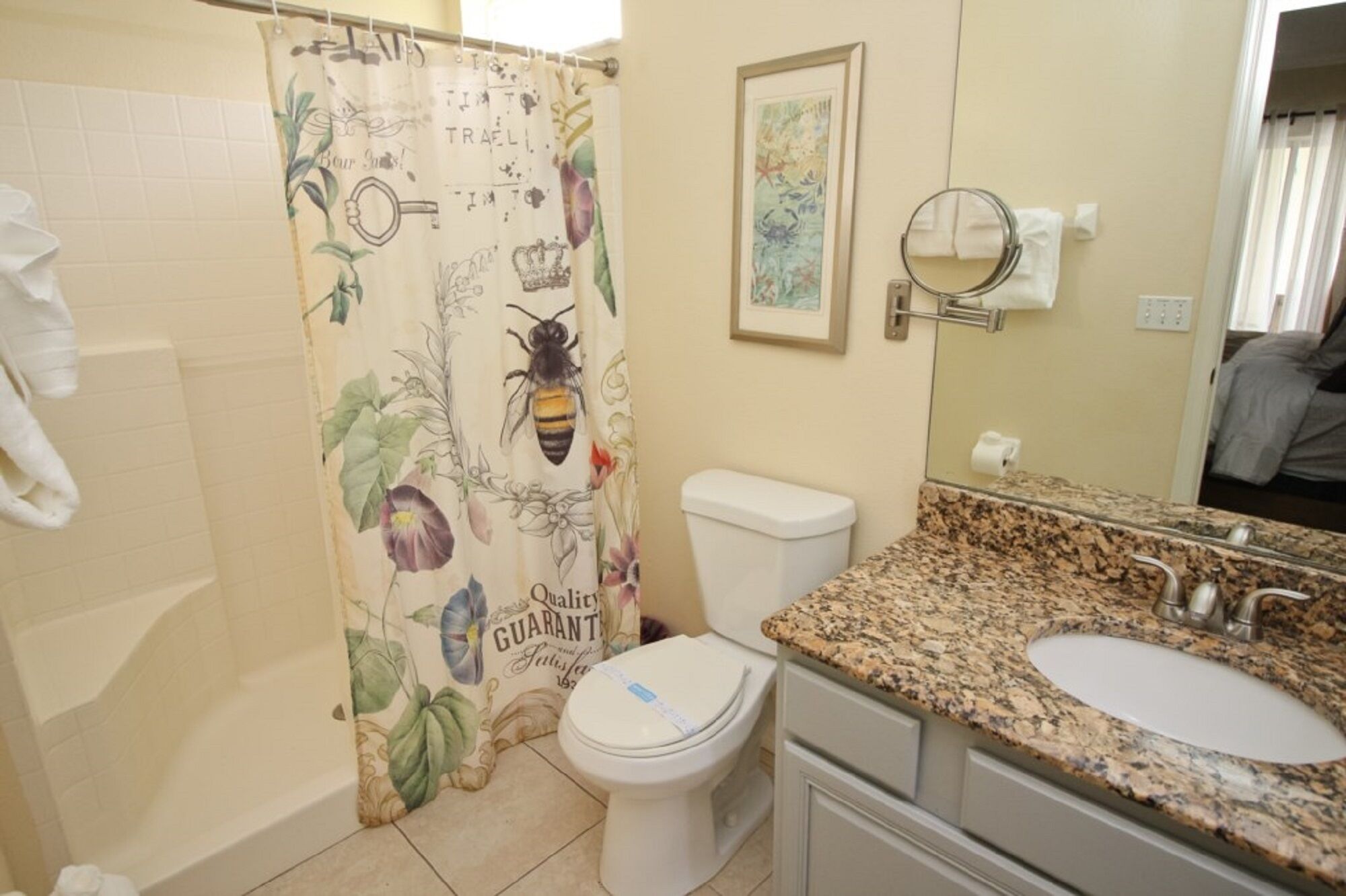 A bathroom with a shower curtain featuring a bee design, a toilet, a sink with a granite countertop, and a framed picture on the wall.