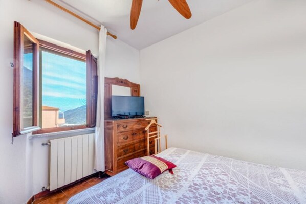 Un dormitorio con un aparador de madera, un televisor encima, una ventana con cortinas y una cama con colcha estampada.