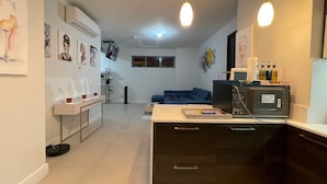 A modern kitchen with a dining area, a blue sofa, and a TV. - Serenity suites (Kingston)