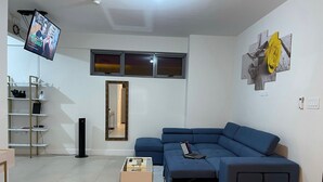 A modern living room with a blue sofa, a coffee table, a TV mounted on the wall, a bookshelf, and a mirror. - Serenity suites (Kingston)
