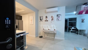 A modern hotel room with a minibar, a desk, a chair, and a TV mounted on the wall. - Serenity suites (Kingston)