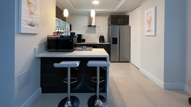 A modern kitchen with a central island, bar stools, a refrigerator, and pendant lighting. - Serenity suites (Kingston)