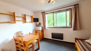 Ein kleiner, gemütlicher Raum mit Holztisch und -stühlen, einem Fernseher, einer Mikrowelle und einem fenster mit Vorhängen.