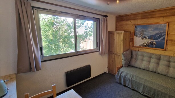 Ein Zimmer mit großem Fenster, einer Holzwand, einer Couch, einem Heizkörper und einem Gemälde.