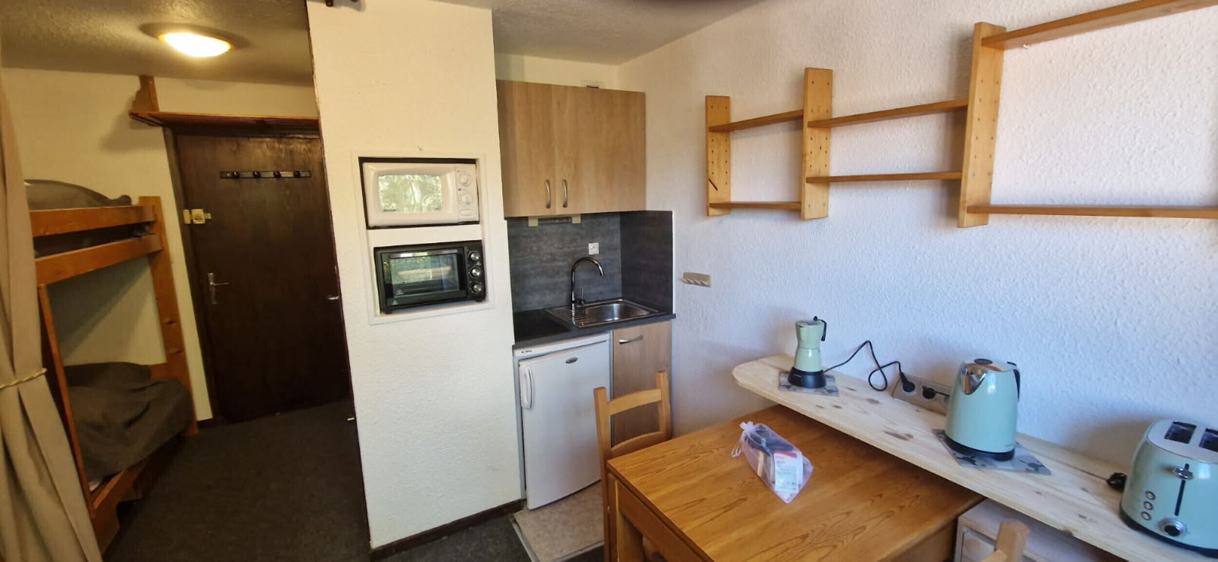 A compact kitchenette with a microwave, oven, sink, and a small table with a kettle and toaster.