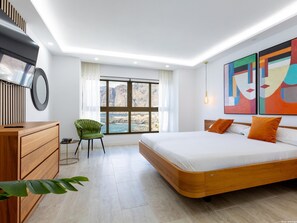 Ein modernes Schlafzimmer mit einem großen Bett, einer hölzernen Kommode, einem grünen Sessel und einem großen Fenster mit Blick auf Klippen.