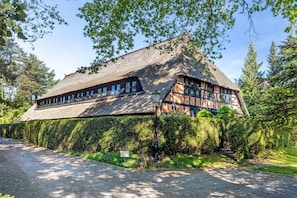 Un bâtiment traditionnel avec un toit de chaume, entouré d’une végétation luxuriante et d’arbres.