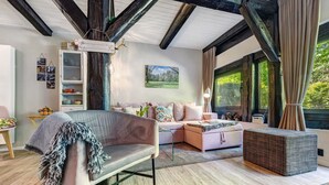 A modern living room with a sofa, a small table, a bookshelf, and a large window. - Apartment 'Wohnen Im Heidehaus' with Private Terrace and Wi-Fi (St. Dionys)