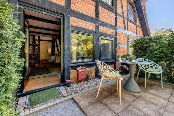 A brick building with large windows, a patio with a table and chairs, and a door leading to an interior space.