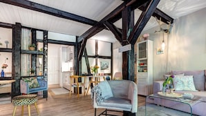 A room with exposed wooden beams, a sofa, a chair, a glass coffee table, and a bookshelf. - Apartment 'Wohnen Im Heidehaus' with Private Terrace and Wi-Fi (St. Dionys)