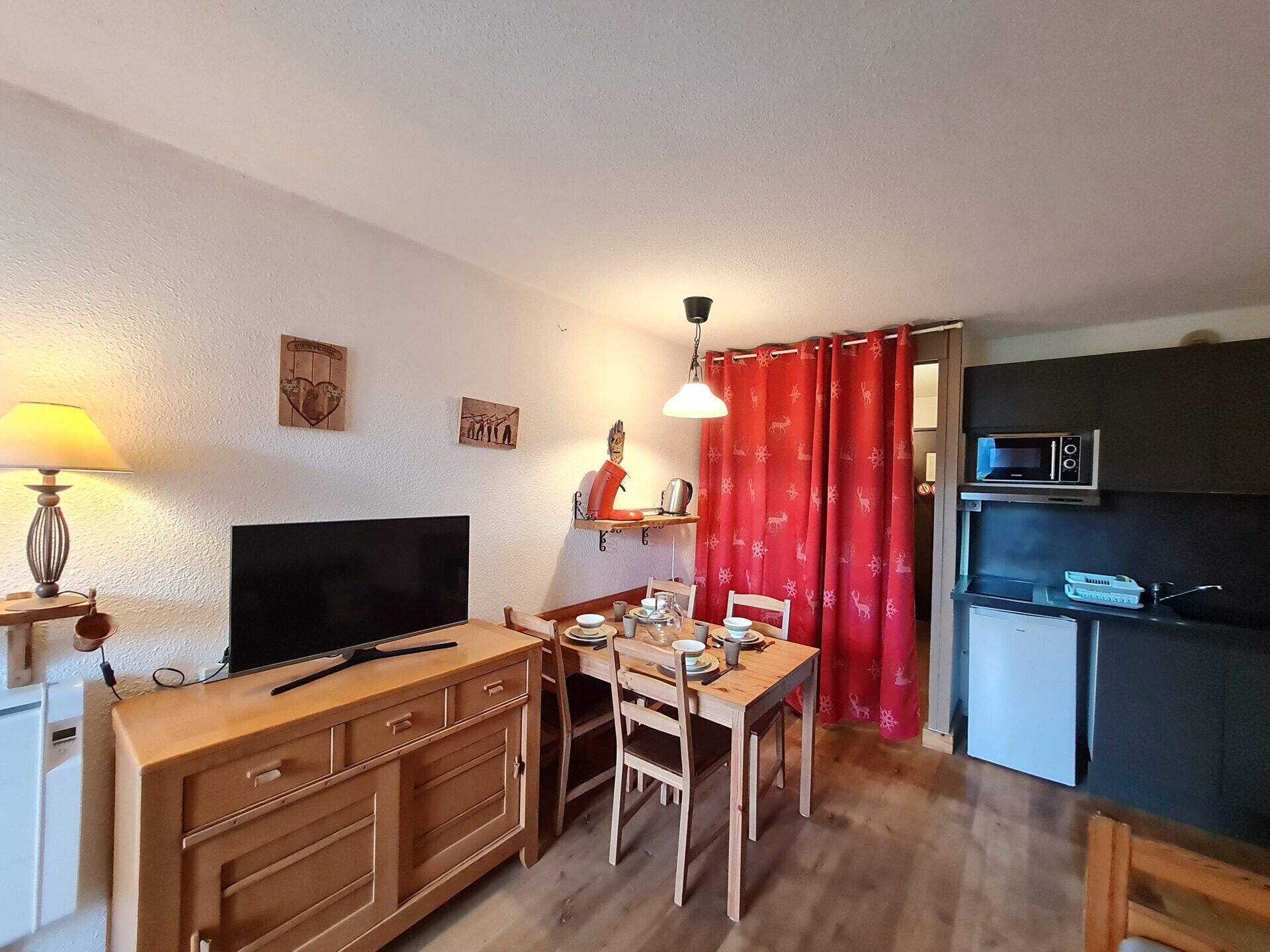 A compact living space with a TV, wooden furniture, a dining table, and a kitchenette.