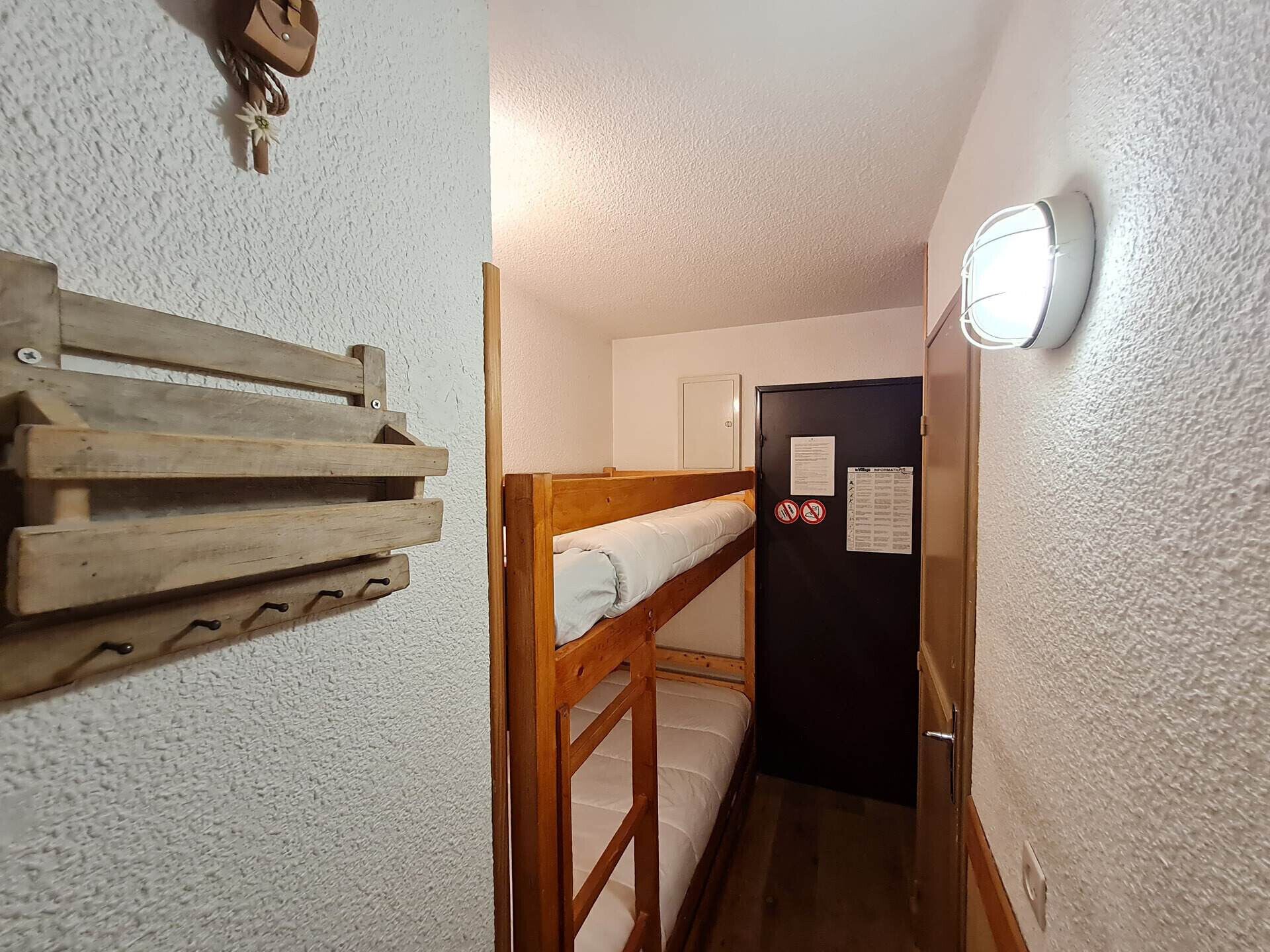 A narrow hallway with a bunk bed, a wooden rack, and a door with a notice.