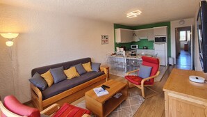 Ein kompakter Wohnraum mit Sofa, Stühlen, einem kleinen Esstisch und einer Küchenzeile.