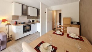 A modern kitchen with white cabinets, a built-in oven, and a microwave. There is a dining table set with plates, glasses, and cutlery.