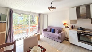 A modern living room with a sofa, dining table, and kitchen area including an oven and a stove.