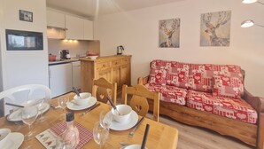 Ein Essbereich mit Holztisch, gedeckt für vier Personen, einer Couch mit gemustertem Bezug und einer Küche im Hintergrund.
