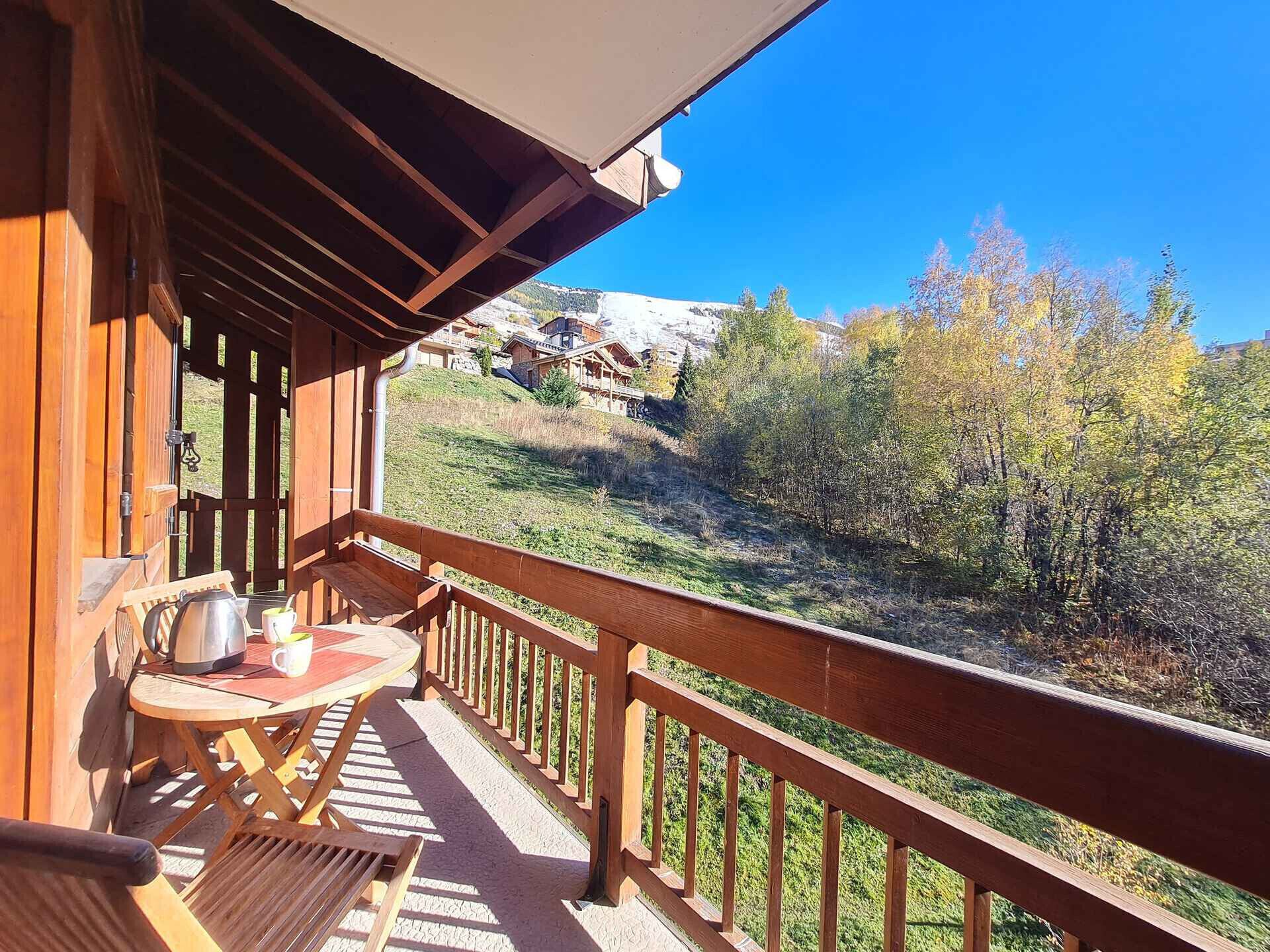 Ein Holzbalkon mit Tisch und Stühlen, der einen Blick auf einen Hügel mit Bäumen und Gebäuden bietet.