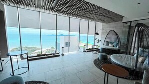 A modern room with large floor-to-ceiling windows, a comfortable seating area with a sofa and chairs, and a small table. - High end condo in popular area with an amazing sea view, 2 min from the beach (Bang Lamung)