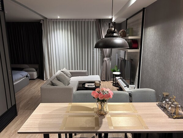 A modern living room with a sofa, a dining table, and a pendant light. - High end condo in popular area with an amazing sea view, 2 min from the beach (Bang Lamung)