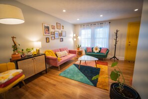 Un salon chaleureux avec un canapé rose, un canapé vert, un fauteuil jaune, une petite table blanche et une plante en pot.