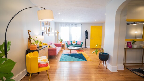 Una sala de estar con un sofá, un sillón, una mesa de centro y una lámpara. Se ve una puerta al fondo.