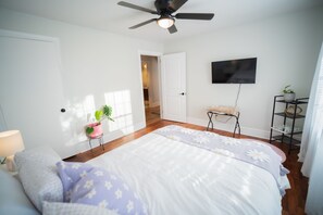 Une chambre à coucher avec un lit, un ventilateur de plafond, une télévision, une plante et une petite table.