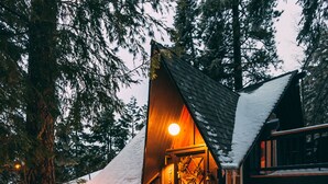 A cabin with a wooden exterior, a staircase leading to a deck, and a snow-covered roof. - Lightfoot Cabin (Running Springs)