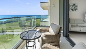 A balcony with a glass table and wicker chairs, overlooking a coastal landscape. - A-502  Stunning studio with balcony (Cupecoy)