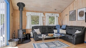 A cozy cabin interior with a black leather sofa, a glass coffee table, and a wood-burning stove.