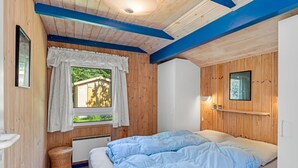 A cozy bedroom with a bed, a window with curtains, a wall-mounted shelf, and a ceiling light.