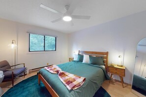 Un dormitorio con cama, una silla, una mesita de noche, un espejo y una ventana.