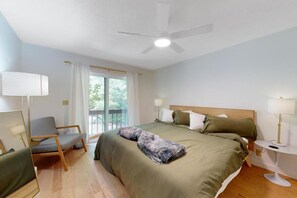 A bedroom with a bed, a chair, a bedside table, a lamp, a ceiling fan, and a window with curtains. - Sage Grove Sanctuary | Hot Tub | Modern | BBQ (East Stroudsburg)