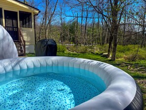 Una piscina inflable con diseño azul y blanco, rodeada por una zona boscosa con árboles y una casa al fondo.