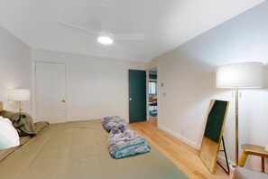 A bedroom with a bed, a standing lamp, a mirror, and a door leading to another room.