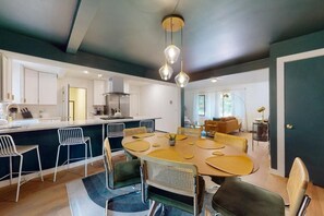 Une cuisine moderne dotée d’un îlot central, d’un coin repas avec une table ronde et des chaises, et d’un espace de vie comprenant un canapé et une table basse.