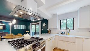 Una cocina moderna con armarios blancos, estufa de acero inoxidable y un ventanal que ofrece luz natural.
