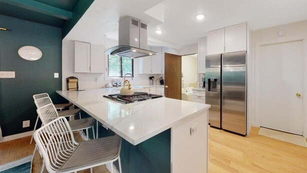 A modern kitchen with white cabinetry, a central island with seating, a stainless steel refrigerator, and a built-in stove.