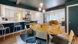 A modern kitchen with a central island, white cabinetry, and a dining area with a round table and chairs.
