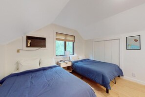 A bedroom with two beds, a window, a radiator, a nightstand, and a door.