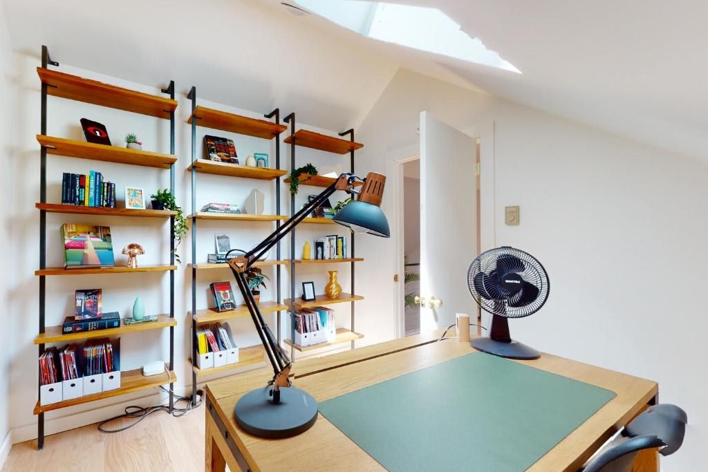 Ein Arbeitsbereich mit Schreibtisch, Schreibtischlampe, Ventilator und zwei Bücherregalen voller Bücher und Dekoration.