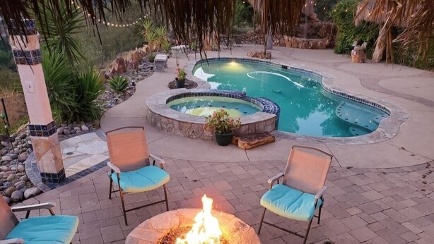 Un jardin avec une piscine, un jacuzzi et un foyer entouré de chaises.